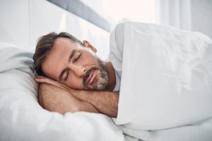 Man sleeping peacefully in white bed linens